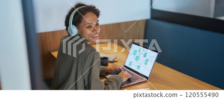 A woman wearing headphones is using a laptop computer at a table 120555490