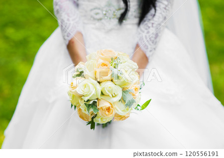 young girl in white wedding dress holding bouquet of flowers and greenery with ribbon.The bride with a wedding bouquet roses. young girl in white wedding dress holding bouquet of flowers and greenery with ribbon.The bride with a wedding bouquet roses. 120556191
