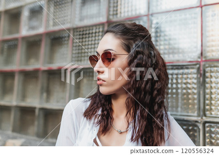 Stylish young woman posing against textured glass wall in urban setting Stylish young woman posing against textured glass wall in urban setting 120556324