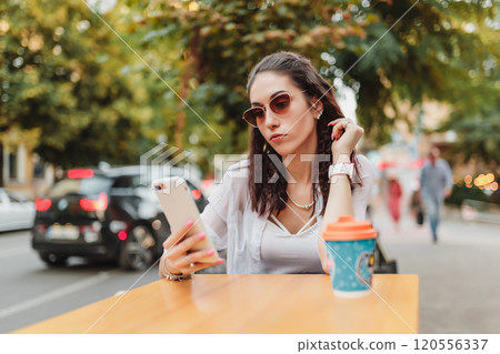 Woman using smartphone at cafe table in city during sunny day Woman using smartphone at cafe table in city during sunny day 120556337