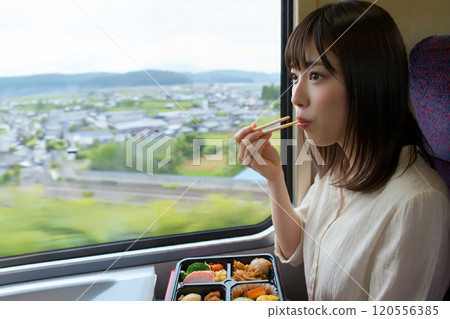 A young woman eating a bento box on a moving train A young woman eating a bento box on a moving train 120556385