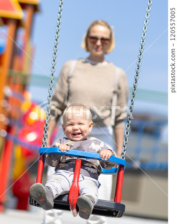 Mother pushing her infant baby boy child on a swing on playground outdoors Mother pushing her infant baby boy child on a swing on playground outdoors 120557005