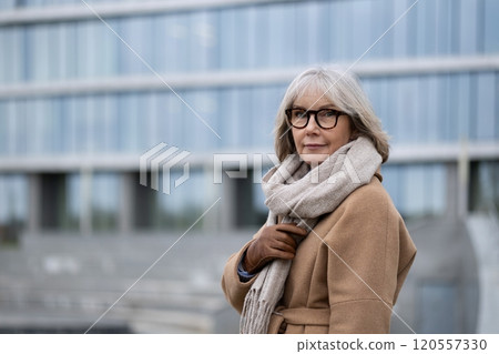 A senior woman stands confidently outdoors wearing a stylish coat and scarf near a modern building A senior woman stands confidently outdoors wearing a stylish coat and scarf near a modern building 120557330