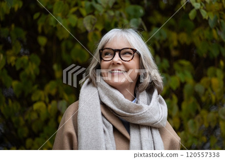 Happy older woman smiles in a cozy scarf while enjoying a sunny autumn day in a vibrant garden with Happy older woman smiles in a cozy scarf while enjoying a sunny autumn day in a vibrant garden with 120557338
