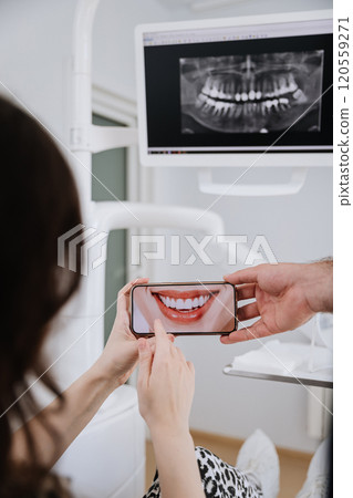 Patient reviewing smile makeover on smartphone with dental Xray displayed in clinic setting Patient reviewing smile makeover on smartphone with dental Xray displayed in clinic setting 120559271
