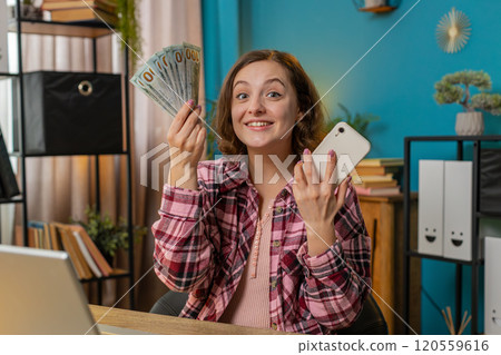 Rich excited woman freelancer looks at camera holding money income earnings cash and smartphone 120559616