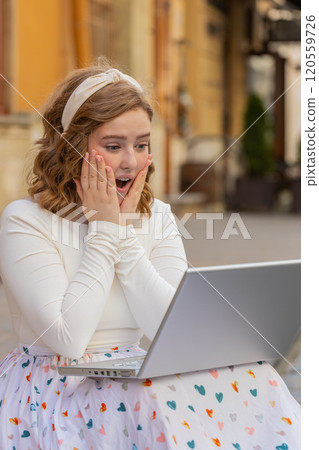 Caucasian happy woman working on laptop celebrate success win money sitting on urban street in city 120559726