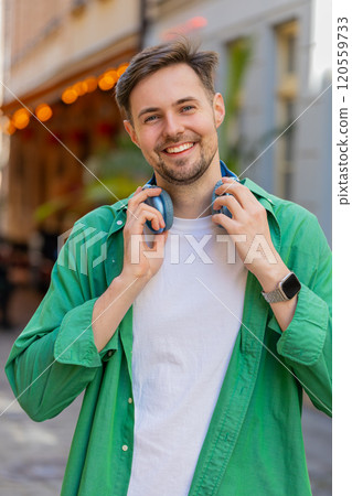 Portrait of smiling young male tourist in casual clothes with wireless headphones around neck 120559733