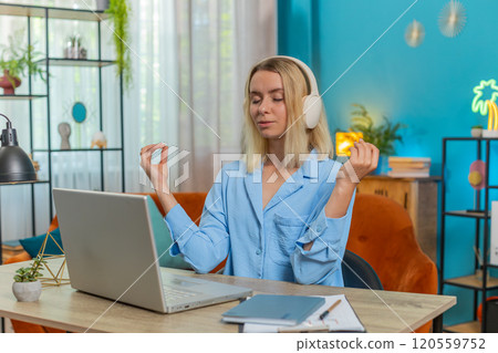Young woman in headphones meditating doing yoga breathing exercise relaxing sitting at home office 120559752