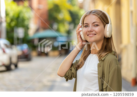 Happy woman in wireless headphones dancing, listening favorite energetic music singing on street 120559859