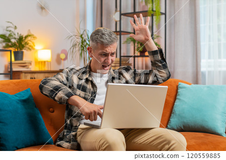 Displeased man use laptop surprised by bad news, virus error, game fail, lottery results at home 120559885