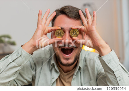 Portrait of happy young male freelancer trader showing bitcoins sitting at home office table 120559954