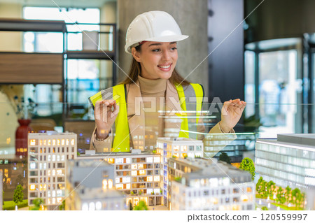 Confident young female architect in hardhat analyzing office complex architectural model in office Confident young female architect in hardhat analyzing office complex architectural model in office 120559997