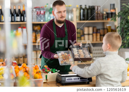 Friendly seller offers cookies to little customer in grocery store Friendly seller offers cookies to little customer in grocery store 120561619