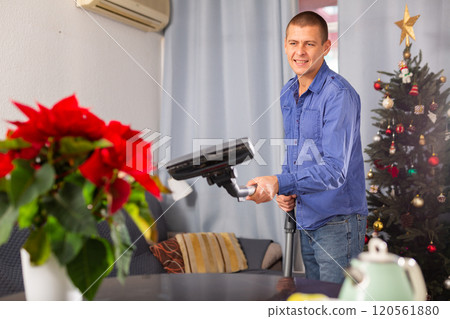 Man vacuuming room in his house before christmas Man vacuuming room in his house before christmas 120561880