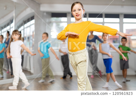 Positive juvenile girl engaged in hip-hop dance in training room with children's group Positive juvenile girl engaged in hip-hop dance in training room with children's group 120561923