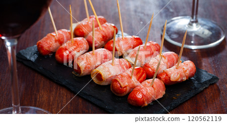 Rolled bacon with sausages on black dish Rolled bacon with sausages on black dish 120562119