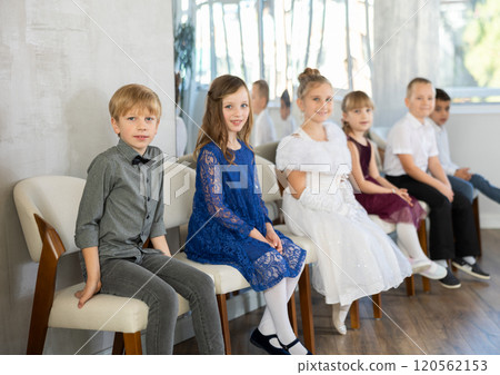 Smiling tweens in festive attire sitting on chairs at school event 120562153