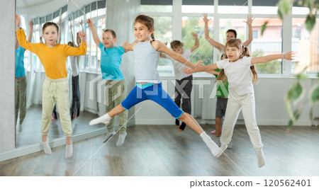 Group of sporty kids with female teacher training in modern dance studio, jumping together Group of sporty kids with female teacher training in modern dance studio, jumping together 120562401