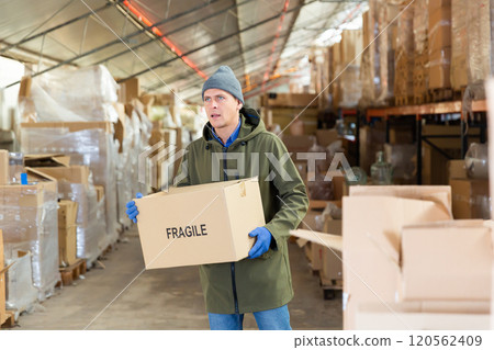 Warehouse worker carrying large box of goods in arehouse 120562409
