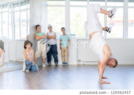 Experienced male trainer demonstrating to group of children dancers correct movements in hip-hop dance in choreography studio 120562457
