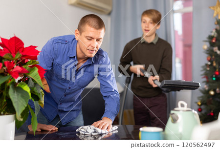 Father wipes the table, son vacuums the room before celebrating new year Father wipes the table, son vacuums the room before celebrating new year 120562497