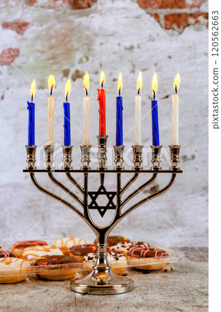 Menorah stands tall with nine colorful candles glowing, surrounded by festive treats decorations as families gather to celebrate Hanukkah joyfully. Menorah stands tall with nine colorful candles glowing, surrounded by festive treats decorations as families gather to celebrate Hanukkah joyfully. 120562663