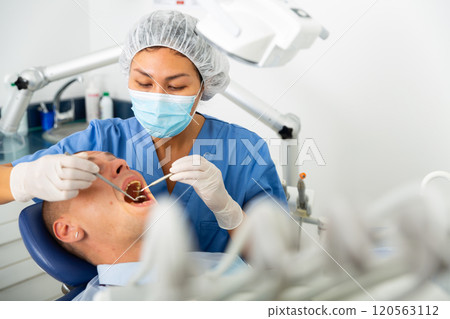Qualified woman dentist in a protective mask treats a man patient 120563112