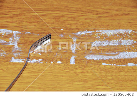 A scene of a woman using a fork to scoop the cream off the film that has been removed from the shortcake and placed on a wooden table. A scene of a woman using a fork to scoop the cream off the film that has been removed from the shortcake and placed on a wooden table. 120563408