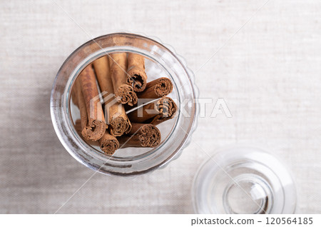 Ceylon cinnamon quills in a glass jar with lid, on linen fabric, with empty space for text. Whole, dried bark strips of Cinnamomum verum, used mainly as aromatic condiment and flavouring additive. 120564185