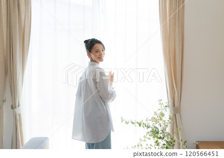 Smiling woman standing by the window in the living room Smiling woman standing by the window in the living room 120566451