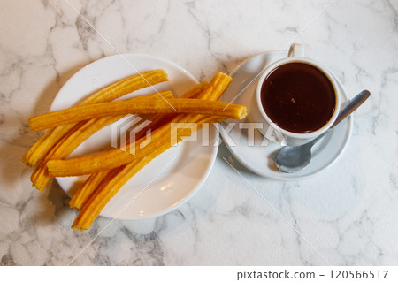 Traditional spanish dessert churros - fried choux pastry and hot chocolate mug on a table Traditional spanish dessert churros - fried choux pastry and hot chocolate mug on a table 120566517