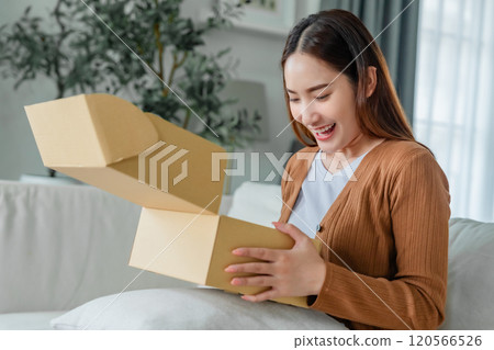Happy young Asian woman opening delivery package at home Happy young Asian woman opening delivery package at home 120566526