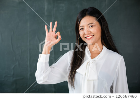 A woman is smiling and giving the thumbs up sign. She is wearing a white shirt and a black tie 120567460