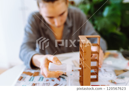 young attractive woman assembling wooden model at table in bright room with house plants 120567623