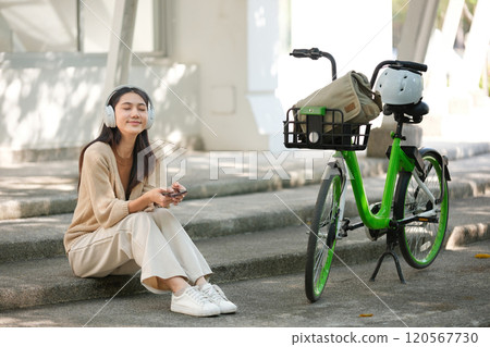 A woman is sitting on a set of stairs with her headphones on 120567730