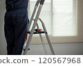 A man in a blue jumpsuit is standing on a ladder. 120567968