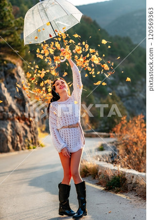 woman umbrella leaves , She holds him over her head, autumn leaves are falling out of him. Beautiful woman in a dress with an umbrella in the autumn park on the road in the mountains. woman umbrella leaves , She holds him over her head, autumn leaves are falling out of him. Beautiful woman in a dress with an umbrella in the autumn park on the road in the mountains. 120569363