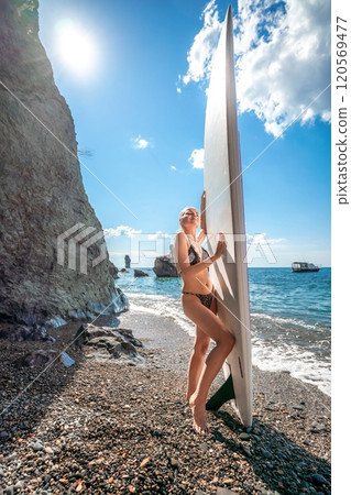 Woman in black bikini sap sea. Portrait of a happy girl on the background of a surfboard in the sea on a sunny summer day 120569477