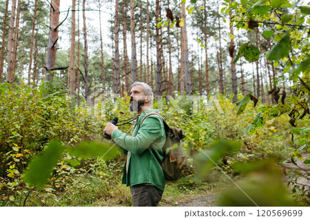 Tourist standing in the middle of nature, using binoculars to observe nature and wildlife in the forest. Tourist standing in the middle of nature, using binoculars to observe nature and wildlife in the forest. 120569699