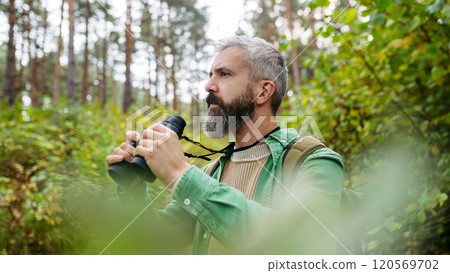 Tourist standing in the middle of nature, using binoculars to observe nature and wildlife in the forest. 120569702