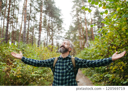 Handsome man standing in the middle of nature with open arms and closed eyes. Peaceful atmosphere of the forest, forestbathing. 120569719
