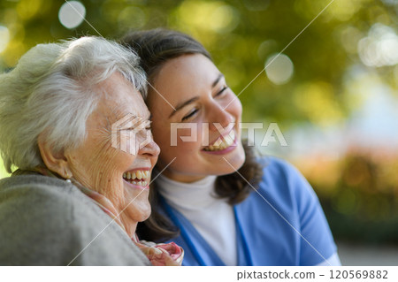 Portrait of nurse and elderly woman in autmn park. Young caregiver spending time with senior patient. 120569882