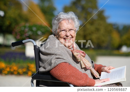 Portrait of elderly woman sitting in wheelchair and reading book. Semale senior spending warm autumn day in city park Portrait of elderly woman sitting in wheelchair and reading book. Semale senior spending warm autumn day in city park 120569887