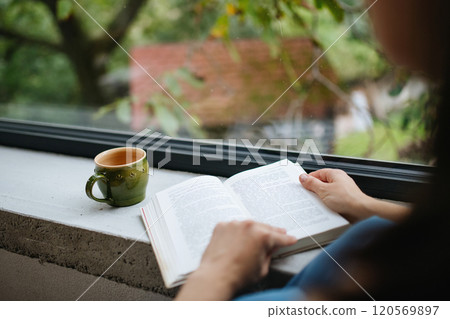 Hygge moment for beautiful woman sitting by a large window with a book. Woman is enjoying time for herself, reading. Hygge moment for beautiful woman sitting by a large window with a book. Woman is enjoying time for herself, reading. 120569897