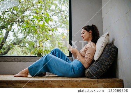 Hygge moment for beautiful woman sitting by a large window with a book. Woman is enjoying time for herself, reading. Hygge moment for beautiful woman sitting by a large window with a book. Woman is enjoying time for herself, reading. 120569898