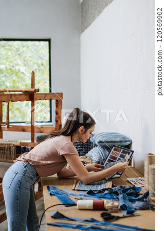 Young businesswoman working on workbench, preparing old fabric for weaving. Upcycled textile, small weaving business and circular economy. Young businesswoman working on workbench, preparing old fabric for weaving. Upcycled textile, small weaving business and circular economy. 120569902