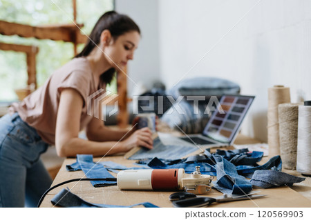 Young businesswoman working on laptop on workbench, standing by wooden loom. Upcycled textile, small weaving business and circular economy. Young businesswoman working on laptop on workbench, standing by wooden loom. Upcycled textile, small weaving business and circular economy. 120569903