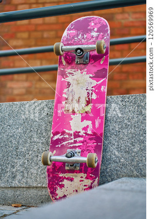 Used scratched pink skateboard against stone wall at city street. Urban sport and youth subculture concept Used scratched pink skateboard against stone wall at city street. Urban sport and youth subculture concept 120569969