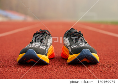 Pair of black and orange running shoes on red running track. Concept of sports training in outdoor setting 120569975
